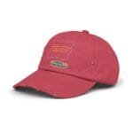 Close-up of a red baseball cap showing a yellow sticker label and a light-blue outline patch on the front, with frayed brim edges.