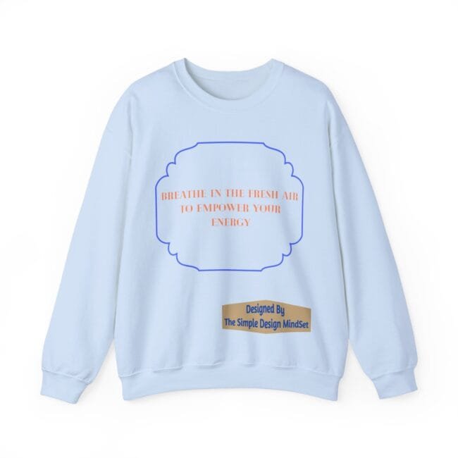 Light blue sweatshirt with an orange quote inside a blue scalloped frame: 'BREATHE IN THE FRESH AIR TO EMPOWER YOUR ENERGY', plus a beige designer label 'Designed By The Simple Design MindSet'.