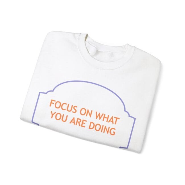 Folded white T-shirt with orange slogan 'FOCUS ON WHAT YOU ARE DOING' inside a purple decorative border.
