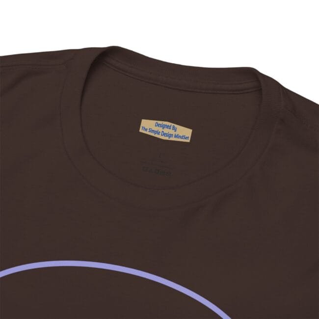 Close-up of a brown t-shirt neckline showing a beige label with blue text: 'Designed By The Simple Design MindSet' near the collar, with part of a lavender arc design visible at the bottom edge.