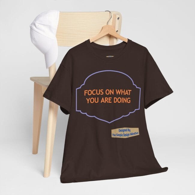 Brown T-shirt on a hanger with a purple framed badge reading 'FOCUS ON WHAT YOU ARE DOING' in orange letters.