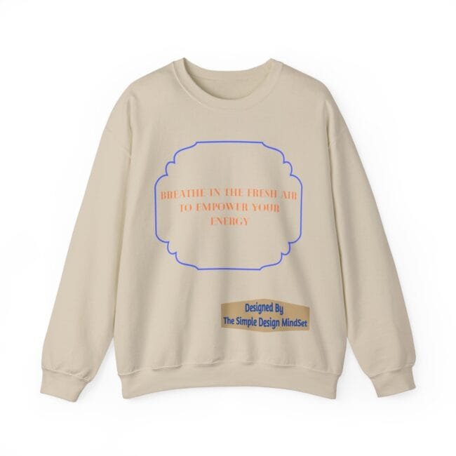 Beige sweatshirt with orange text inside a blue decorative frame: 'BREATHE IN THE FRESH AIR TO EMPOWER YOUR ENERGY'; designer label below.