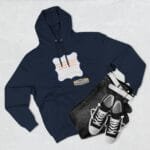 Navy hoodie with a pale purple decorative label graphic on the chest, paired with dark jeans and white‑trimmed black sneakers for a casual outfit.