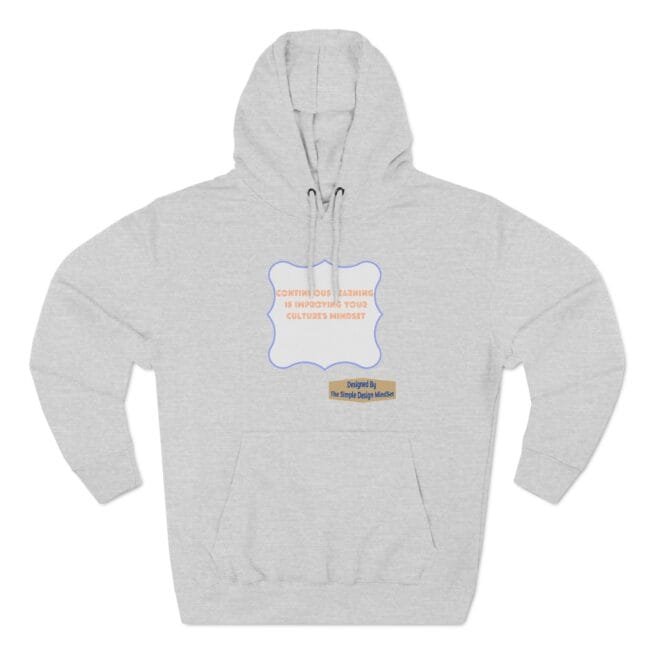 Grey hoodie with a decorative blue-bordered label on the chest, containing orange text about continuous learning and culture. A small tan label at the lower right reads 'Designed By The Simple Design Mind' (brand credit).