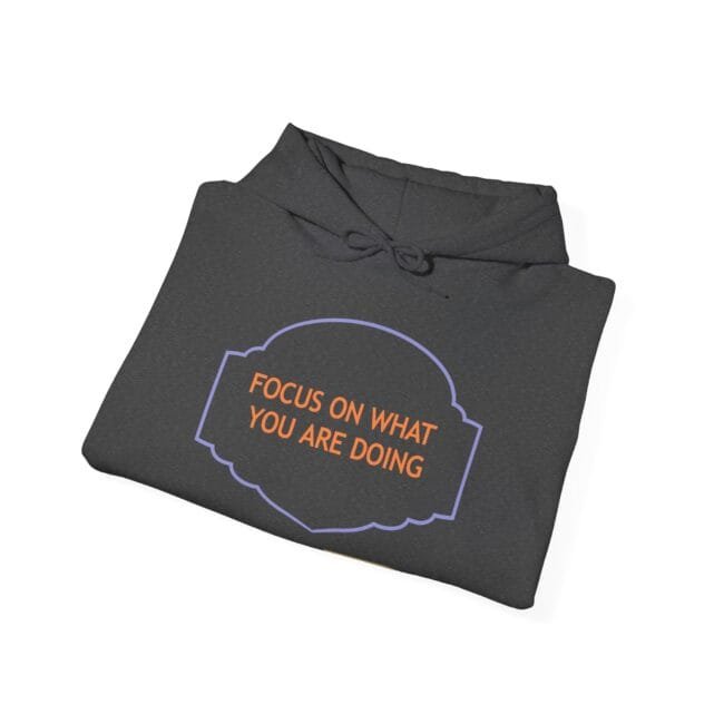 Folded charcoal hoodie with orange text 'FOCUS ON WHAT YOU ARE DOING' inside a purple decorative frame on the front.