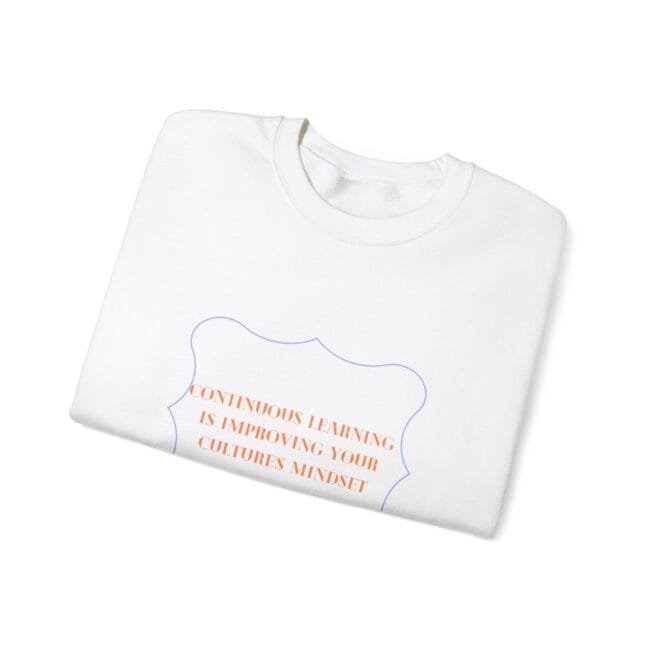 White folded t-shirt with an orange slogan inside a blue decorative badge: 'CONTINUOUS LEARNING IS IMPROVING YOUR CULTURE'S MINDSET'