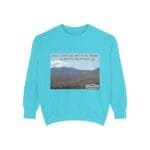 Turquoise sweatshirt with a desert landscape graphic and the words: 'Take a coffee or juice in the desert to resolve the problem' across the top; small label in the bottom-right corner.