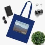 Blue tote bag laid flat with a desert landscape print and slogan on the front panel.