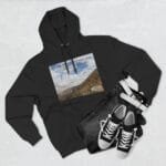 Black hoodie laid flat with a rectangular mountain landscape graphic on the chest and faint inspirational text across the top of the image area, paired with jeans and sneakers as accessories in the scene.