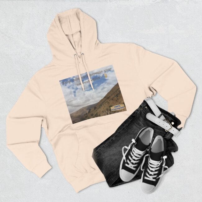 Beige hoodie with a square mountain landscape graphic on the chest, paired with dark jeans and black‑white sneakers laid flat.