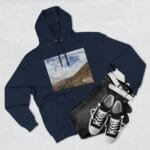 Navy hoodie with a landscape-print graphic on the chest, laid beside black denim jeans and white sneakers on a light background (flat lay).