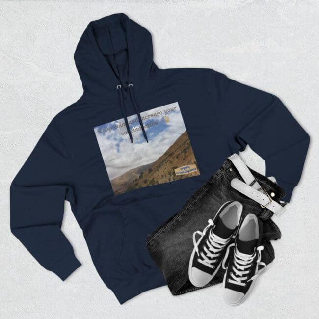 Navy hoodie with a landscape-print graphic on the chest, laid beside black denim jeans and white sneakers on a light background (flat lay).