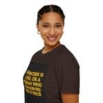 Smiling woman with braided hair wearing a dark brown T-shirt that reads: 'A princess is a girl or a woman who conserves her ethics.'