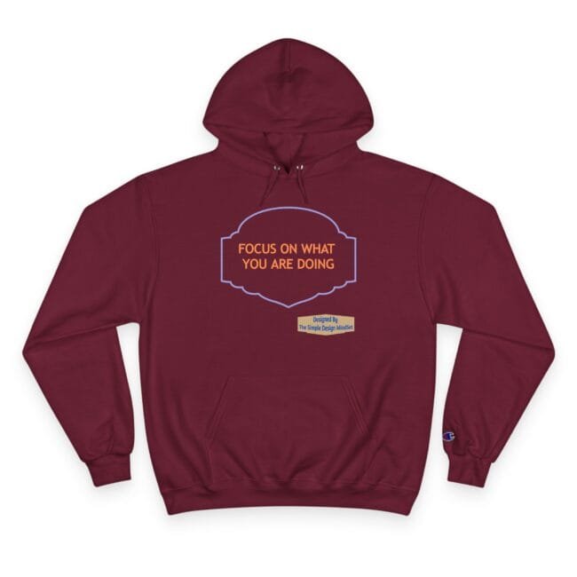 Maroon hooded sweatshirt with orange text 'FOCUS ON WHAT YOU ARE DOING' inside a blue decorative frame, chest area.