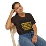Woman seated on a wooden chair, smiling, wearing a brown T‑shirt with a neon ethics slogan.