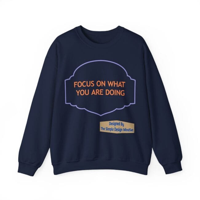 Navy sweatshirt with orange motto 'FOCUS ON WHAT YOU ARE DOING' in a purple decorative frame and a beige credit banner below.