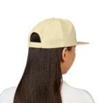 Back view of a pale yellow baseball cap on a person with long dark hair, showing the adjustable strap at the back and a curved brim