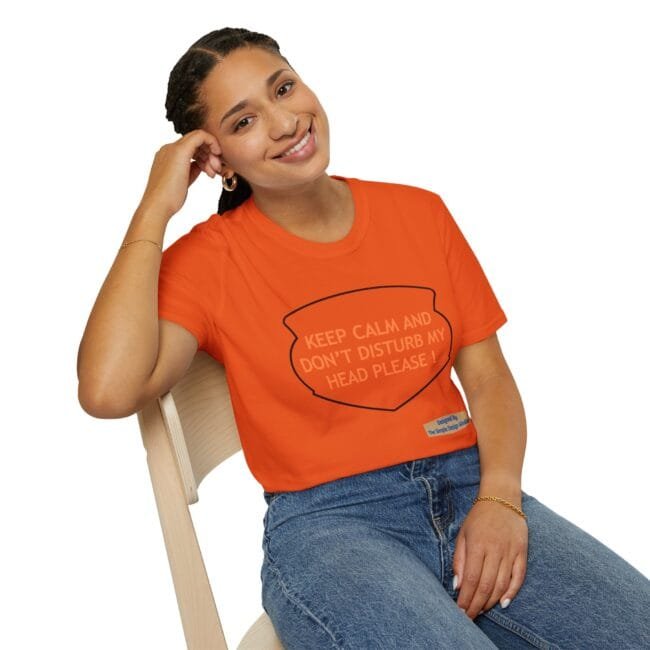 Smiling woman in an orange t-shirt seated on a chair, with text reading 'KEEP CALM AND DON'T DISTURB MY HEAD PLEASE!' on the shirt