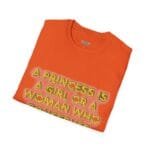 Orange folded T-shirt featuring a neon-yellow outlined slogan: 'A PRINCESS IS A GIRL OR A WOMAN WHO'