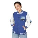 Young woman wearing a blue and white varsity jacket with patch on chest, hands in pockets, smiling at camera.