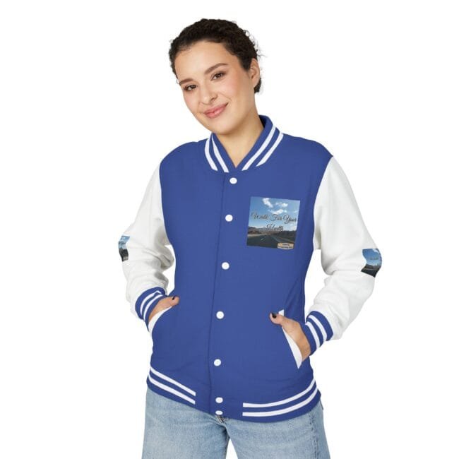Young woman wearing a blue and white varsity jacket with patch on chest, hands in pockets, smiling at camera.