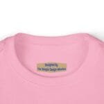 Close-up of a pink shirt neckline with a tan brand tag reading 'Designed By The Simple Design MindSet'