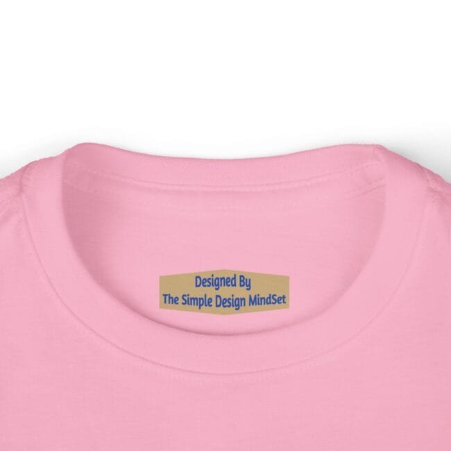 Close-up of a pink shirt neckline with a tan brand tag reading 'Designed By The Simple Design MindSet'
