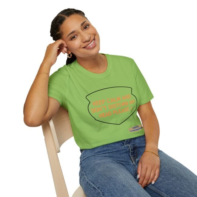 Smiling woman wearing a lime green T-shirt with an orange slogan, seated on a wooden chair outdoorsy style. The shirt reads, 'KEEP CALM AND DON'T DISTURB MY HEAD PLEASE!'