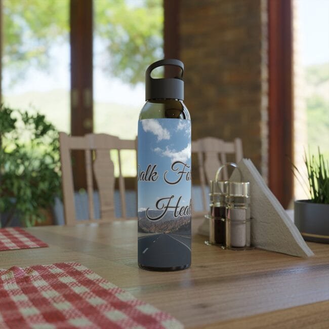 Water bottle on a wooden table with a label showing a blue sky and road and the text 'Walk Far Health' in a cozy dining area.