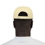 Back view of a person wearing a pale yellow baseball cap with an adjustable strap at the back on a white shirted figure.