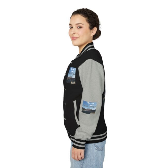 Side view of a woman wearing a black and gray varsity jacket with striped cuffs and patches on the chest and sleeve, standing against a white background, in profile.