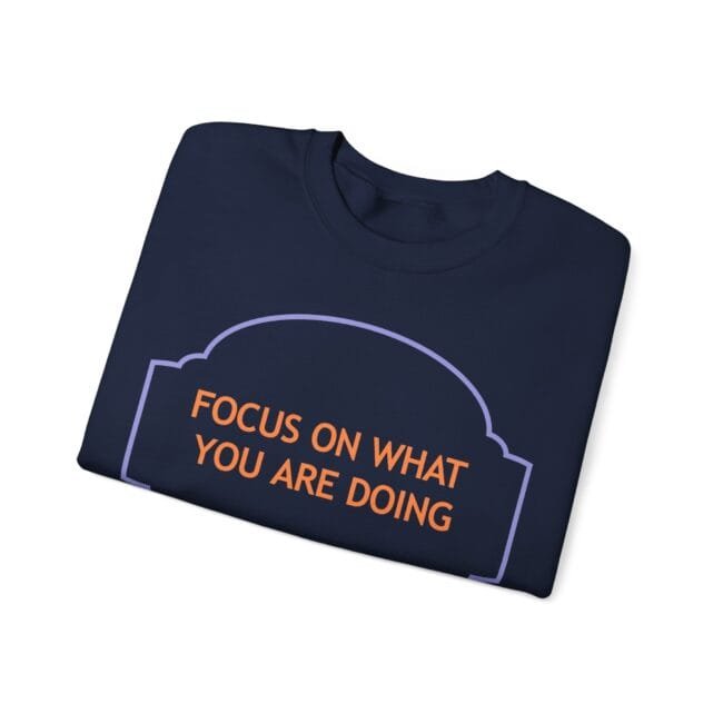Navy folded t-shirt with orange text 'FOCUS ON WHAT YOU ARE DOING' inside a purple decorative frame.