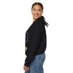 Side view of a smiling woman wearing a black sweatshirt and blue jeans, with braided hair and gold hoop earrings.