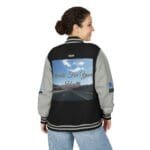 Back view of a woman wearing a black and gray varsity jacket with a large back panel showing a highway scene and the text 'Walk For Your Health'.