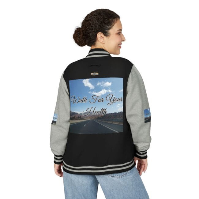 Back view of a woman wearing a black and gray varsity jacket with a large back panel showing a highway scene and the text 'Walk For Your Health'.