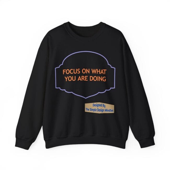 Black sweatshirt with an orange quote 'FOCUS ON WHAT YOU ARE DOING' inside a purple decorative frame and a beige designer tag at the bottom left.