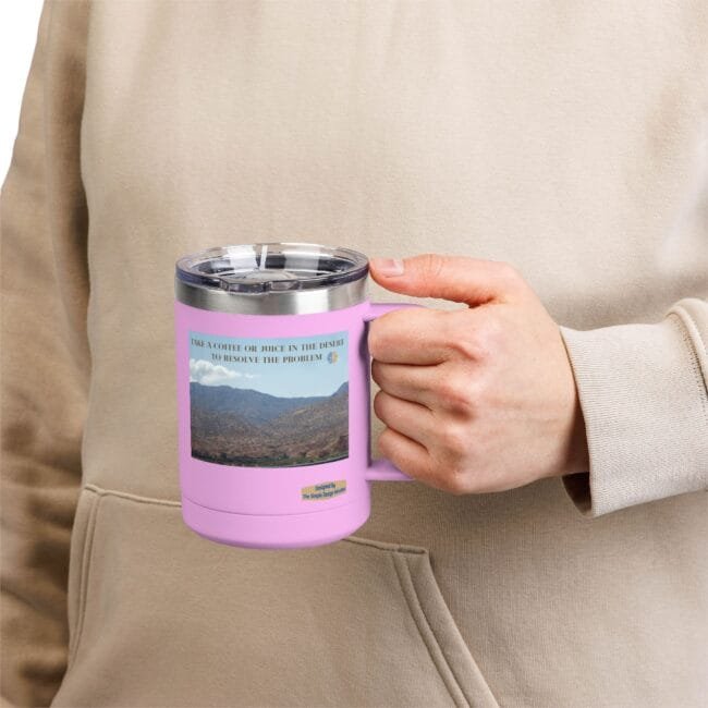 Pink insulated mug with a landscape photo and label, held by a person in a beige hoodie outside the frame.
