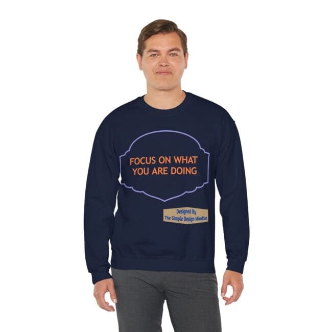 Man wearing a navy sweatshirt with an orange slogan, 'FOCUS ON WHAT YOU ARE DOING', inside a purple outlined badge on the chest.