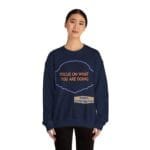 Navy sweatshirt on a woman with an orange message, 'FOCUS ON WHAT YOU ARE DOING,' inside a purple decorative frame.