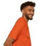 Smiling man with curly hair and beard wearing an orange T-shirt, facing right, against a white background.