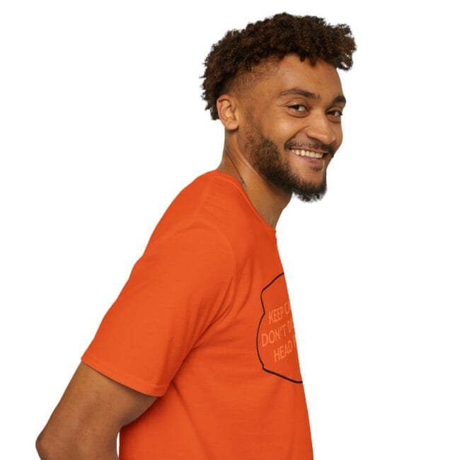 Smiling man with curly hair and beard wearing an orange T-shirt, facing right, against a white background.