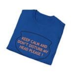 Blue folded t-shirt with orange text 'KEEP CALM AND DON'T DISTURB MY HEAD PLEASE!' inside a speech-bubble outline.
