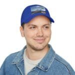 Smiling man in a denim jacket wearing a bright blue cap with a 'Walk For Your Health' patch, looking to the side.