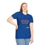 Woman wearing a blue T-shirt with an orange slogan: 'Keep calm and don’t disturb my head please!' on a shield graphic, smiling.