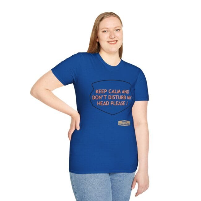 Woman wearing a blue T-shirt with an orange slogan: 'Keep calm and don’t disturb my head please!' on a shield graphic, smiling.