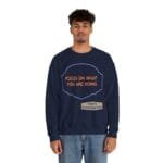 Model wearing a navy sweatshirt with an orange quote reading 'FOCUS ON WHAT YOU ARE DOING' and a small tan label 'Designed By The Simple Design MindSet'