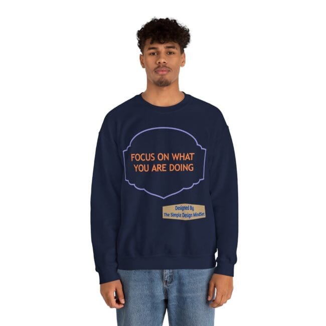 Model wearing a navy sweatshirt with an orange quote reading 'FOCUS ON WHAT YOU ARE DOING' and a small tan label 'Designed By The Simple Design MindSet'