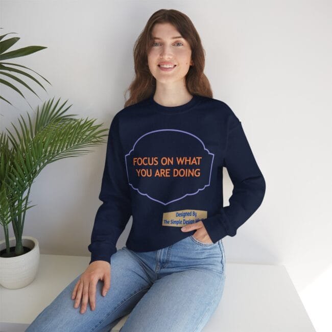 Woman sitting on a white surface wearing a navy sweatshirt with orange text: 'FOCUS ON WHAT YOU ARE DOING'.