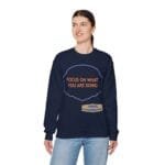 Woman wearing a navy sweatshirt with orange text 'FOCUS ON WHAT YOU ARE DOING' and a small designer label at the hem.