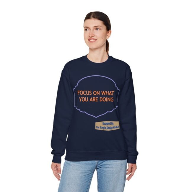Woman wearing a navy sweatshirt with orange text 'FOCUS ON WHAT YOU ARE DOING' and a small designer label at the hem.